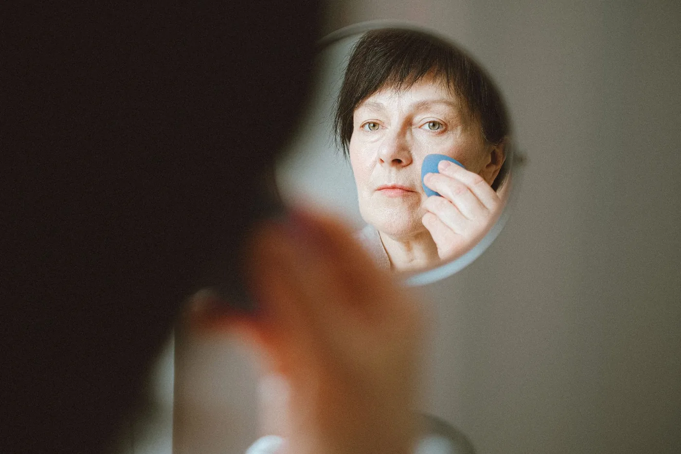 Žena si nanáší make up před zrcadlem v přirozeném světle.